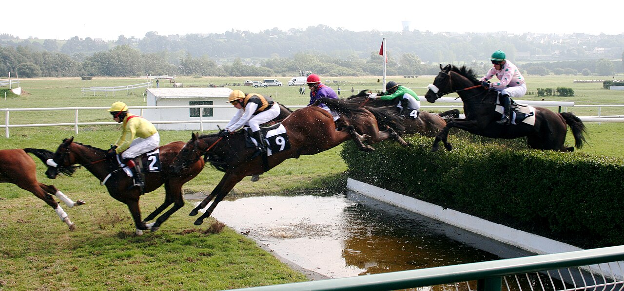 Runners kicking up wet turf on a rain-softened track during a monsoon meeting